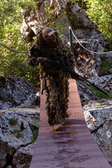 A military man or airsoft player in a camouflage suit sneaking the rope bridge and aims from a sniper rifle to the side or to target. 