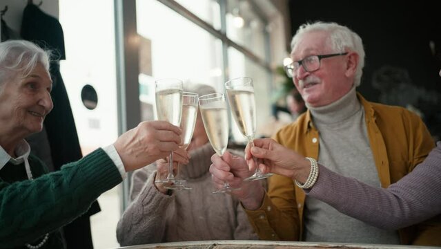 Happy senior friends sitting indoors in cafe clinking champagne glasses and celebrating