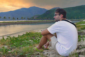 Fototapeta na wymiar Upset man sitting at beach and watching sunset in tropics of Vietnam