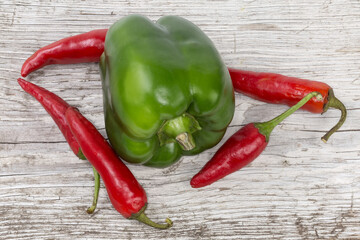 Green bell pepper and red chillies on wooden cracked surface