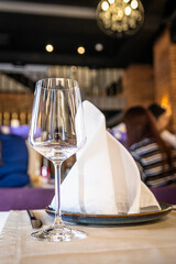 Empty wine glass on the table in front of the napkin on a plate. Restaurant serving.