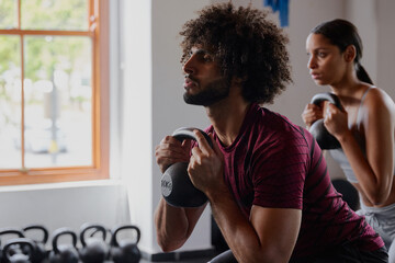Young middle eastern man and biracial woman doing kettlebell squats at the gym - Powered by Adobe