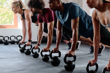 Group of resilient young adults doing plank exercise with kettlebell at the gym