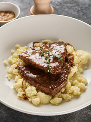 Close up view of sliced roasted beef with mashed potato on plate over grey background