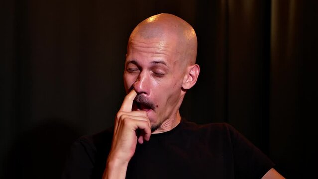 a bald young man in a black t-shirt in a dark room first looks into the frame and then starts picking his nose hard
the concept of bad habits in modern society
the question of benefit or disgust from 