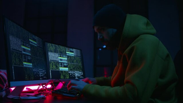 Young man hacker by computer in the dark room at night, cyberwar concept.