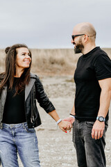 Portrait of happy    smiling  Couple standing on cliff against sea during  the winter .Young happy Bearded muscular  man  ikissing and hugging beautiful woman  in leather jacket and hat on a beach