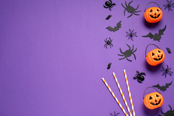 Flat lay composition with plastic pumpkin baskets, paper bats, spiders and cocktail straws on purple background, space for text. Halloween decor