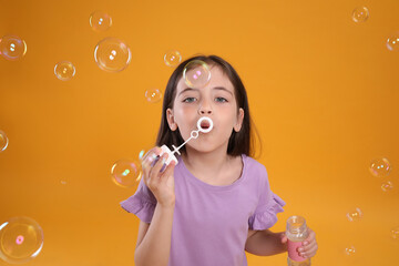 Little girl blowing soap bubbles on yellow background