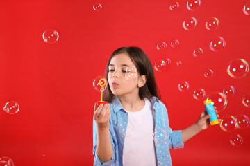 Fototapeta premium Little girl blowing soap bubbles on red background