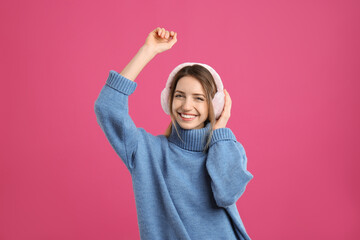 Happy woman wearing warm earmuffs on pink background