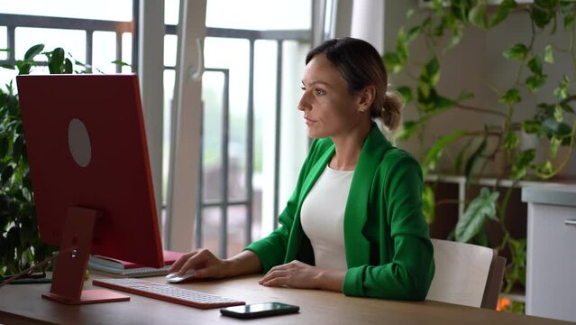 Young European woman is having problems with wrist due to working long with computer mouse and keyboard. Girl sits at office desk stretches wrists due to pain associated with tunnel with syndrome