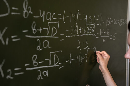 female hand writing math formulas on the classboard