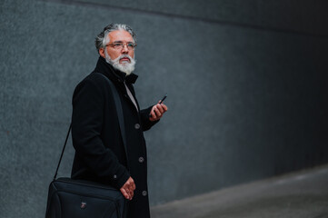 Portrait of a senior businessman using smartphone outside of the office building