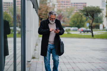 Portrait of a senior businessman using smartphone outside of the office building