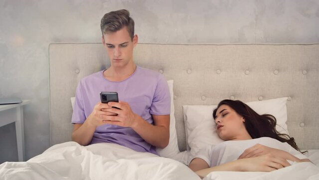 Man Chatting on Phone While Girl is Sleeping. Man Using Phone in Bed. Girl Sleeping in bed. Shot on RED