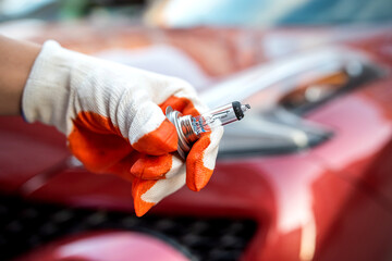 halogen bulb in a man's hand against the background of the headlights of a beautiful car