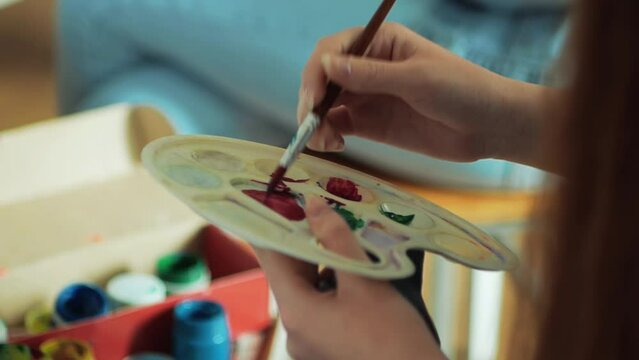 female artist  with brush mixes paint in palette while drawing picture in art studio close-up
Coloring the color compatibility for the artist.