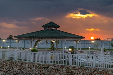 View of a wedding place with flowers arch, lamps, and other ornaments under the orange sunset sky