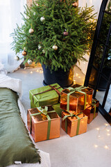 New Year's gifts in paper and bright ribbons under the Christmas tree on the floor on New Year's Eve. A Christmas tree decorated with toys stands by the bed