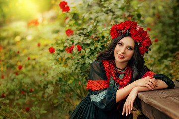 Close-up portrait Ukrainian happy girl looks at camera. Authentic woman smiling face. National ethnic vintage costume black dress stylish vyshyvanka. Wreath crown on head red flowers roses, poppies - obrazy, fototapety, plakaty
