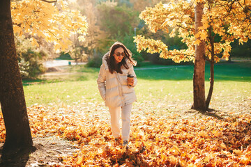 Woman with coffe cup walking in the autumn park