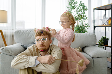 Cute daughter making hairstyle for exhausted father
