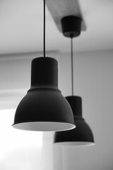 Vertical grayscale shot of minimalistic black lamps hanging from a ceiling