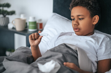 Obraz premium Sick boy lying in bed with fever and checking temperature