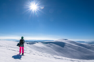 Snowboarder woman with snowboard in hand on mountain top. Winter freeride snowboarding