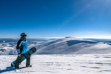 Snowboarder with snowboard in hand on mountain top. Winter freeride snowboarding