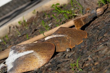 Closeup shot of rusted shovels and a rusted pick axe laid out on the ground