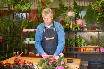 Älterer Gärtner als Inhaber im Blumenladen mit Computer