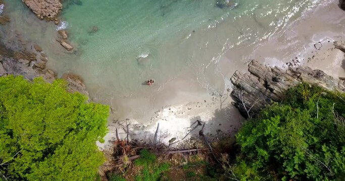 Aerial Overhead View Of Couple Walking Into Waters From Secluded Cove Beach
