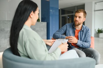 Psychologist talking with patient on therapy session. Depressed man speaking to a therapist while she is taking notes.