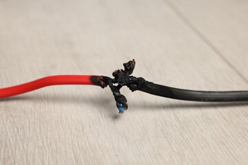 Burnt red wire on wooden floor, closeup. Electrical short circuit