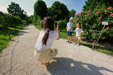  Mother takes photos of children in the garden on her phone.