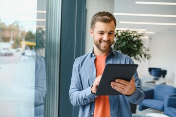 Fototapeta premium Portrait of young businessman with tablet standing in an office, working.