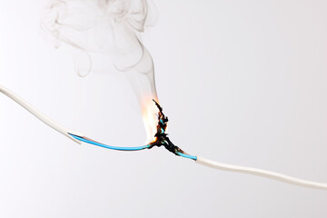 Inflamed white wire on grey background, closeup. Electrical short circuit
