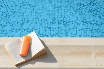 Open book and sunscreen on swimming pool edge, above view. Space for text
