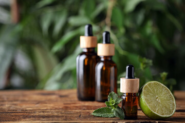 Bottles of essential oil, lime and fresh mint on wooden table against blurred background. Space for text
