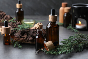 Bottles of juniper essential oil and twigs on grey table