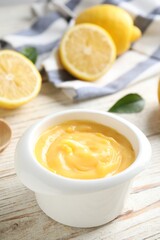 Delicious lemon curd in bowl on white wooden table, closeup