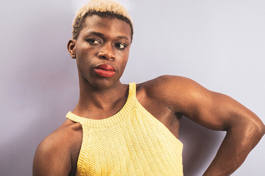 An androgynous young man posing on a purple background while wearing a yellow t-shirt. Androgynous.
