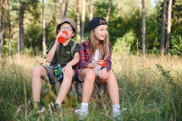Fototapeta premium boy and girl go hiking with backpacks on forest road bright sunny day