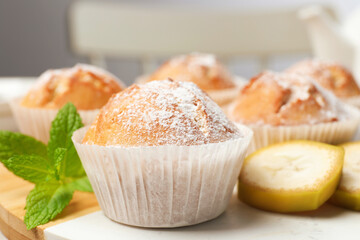 Tasty muffins served with mint and banana on board, closeup
