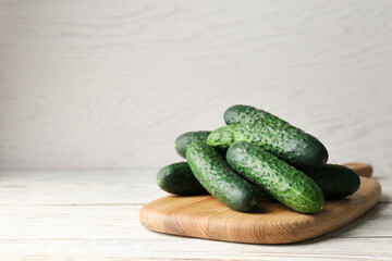Board with fresh ripe cucumbers on white wooden table, space for text