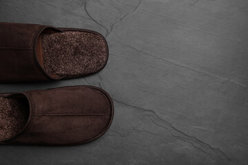 Pair of brown slippers on dark grey floor, top view. Space for text