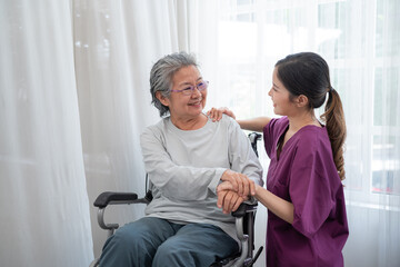 Asian young nurse taking care and talking mature female patient sitting on wheelchair in hospital. Healthcare concept.