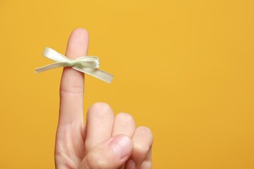 Woman showing index finger with tied bow as reminder on orange background, closeup. Space for text